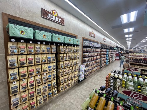 A grocery store aisle featuring shelves of jerky products and various snacks, with bright lighting and organized displays.