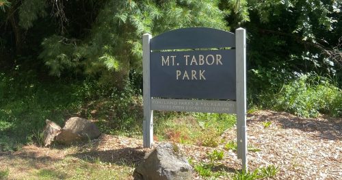 Sign for Mt. Tabor Park surrounded by greenery, with a path leading into the park.