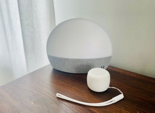 A modern speaker and a small portable speaker on a wooden surface, with soft natural light in the background.