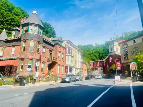 A charming street scene featuring historic buildings, flags, and greenery under a clear blue sky.