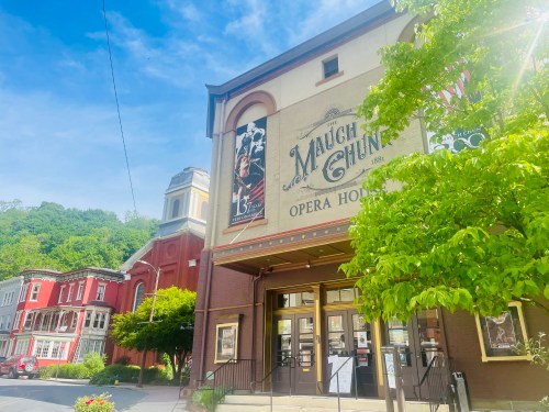 Historic opera house with a colorful facade, surrounded by greenery and charming buildings under a clear blue sky.
