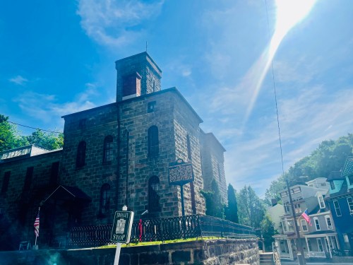 Historic stone building under a bright blue sky, with a stop sign in the foreground and trees in the background.