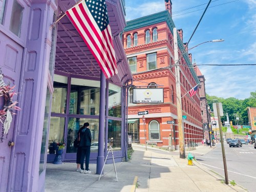 A person stands outside a purple building with American flags, near a street sign in a historic town.