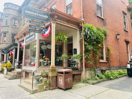 A charming storefront with a sign reading "Somersault," featuring plants and colorful decorations on a brick building.