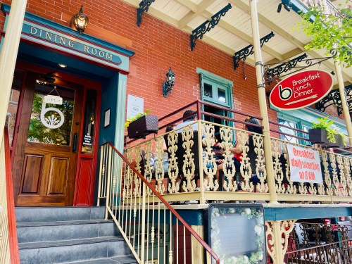Entrance to a restaurant with a sign for breakfast, lunch, and dinner, featuring a decorative balcony and stairs.