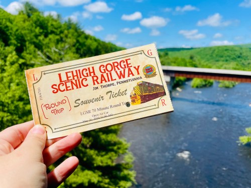 A hand holds a vintage Lehigh Gorge Scenic Railway ticket over a river and green landscape.
