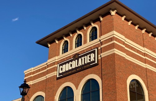 A brick building with a sign reading "Chocolatier Restaurant, Bar & Patio" against a clear blue sky.