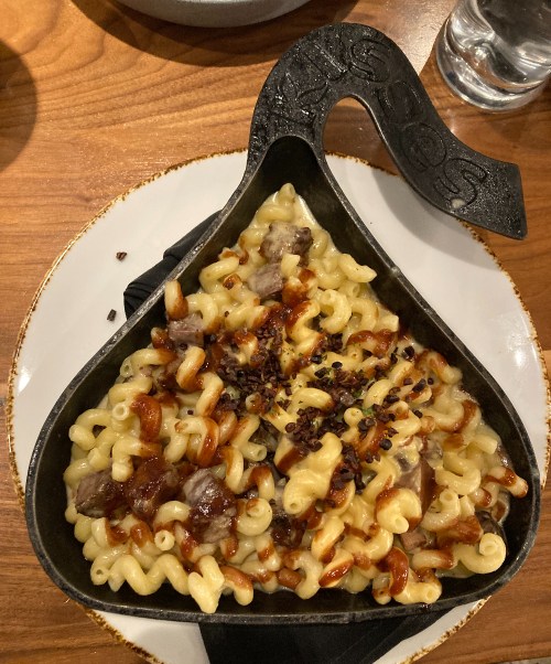 A cast iron dish filled with macaroni, topped with meat and a crispy garnish, served on a wooden table.