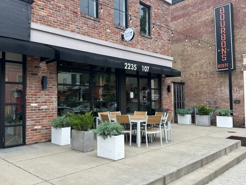Exterior of a restaurant with a brick facade, outdoor seating, and planters, featuring a sign that reads "Bourbon's Bistro."