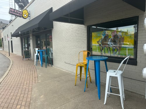 Outdoor seating area with colorful chairs and tables in front of a doughnut shop, featuring a horse racing mural.