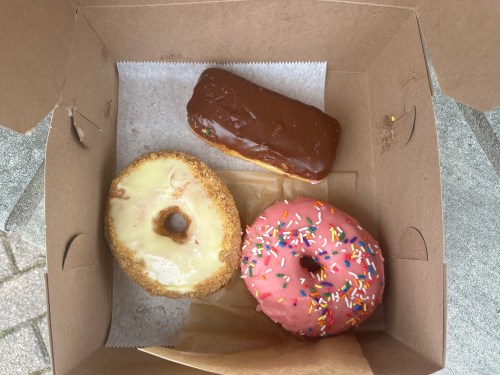 A box containing three donuts: a glazed donut, a chocolate-covered bar, and a pink frosted donut with sprinkles.