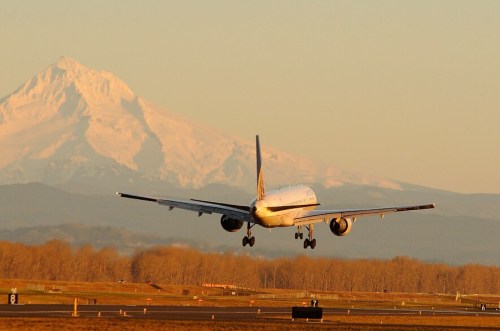 A plane landing on a runway with a snow-capped mountain in the background during sunset.