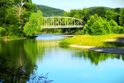 A serene river scene with a green bridge, surrounded by lush trees and reflecting in the calm water.