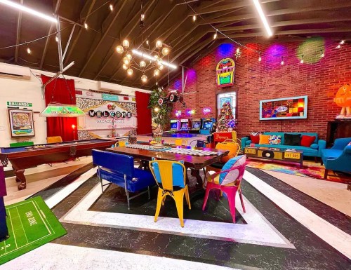 A vibrant arcade room featuring colorful furniture, a pool table, and retro arcade games under a stylish ceiling.