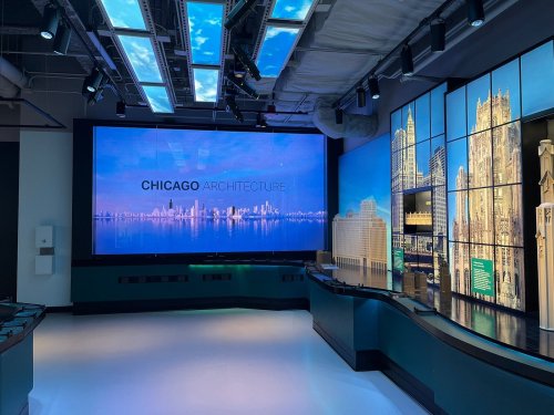 A modern exhibit space featuring a large screen displaying "Chicago Architecture" with city skyline visuals.