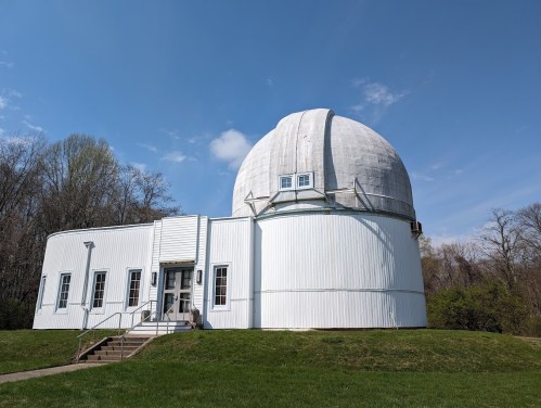 A white observatory building with a large dome, set against a clear blue sky and surrounded by greenery.