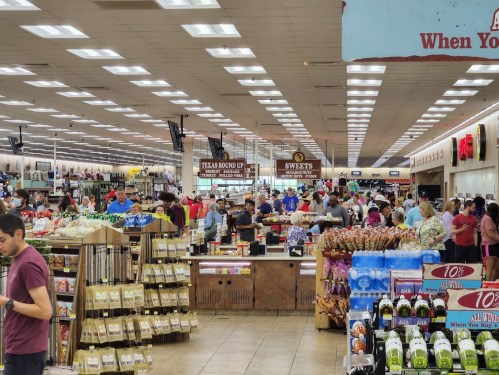 A busy store interior filled with shoppers, showcasing various products and signs, with a bright, spacious layout.
