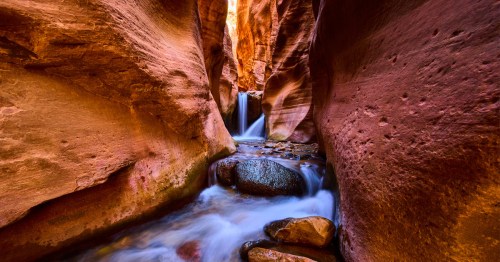 Kanarra Falls waterfall, shown through a narrow slot canyon with stunning red walls.