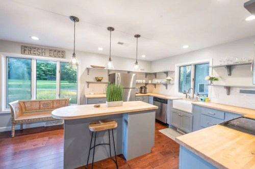 Modern kitchen with gray cabinets, wooden countertops, and large windows overlooking a green landscape. Fresh eggs sign above.