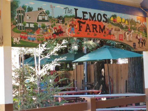 Colorful mural of Lemos Farm featuring animals, a train, and farm scenes, with green umbrellas in the foreground.