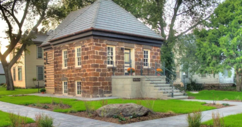 A small stone house with a sloped roof, surrounded by a landscaped garden and pathway.