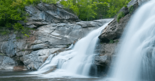 A serene waterfall cascading over rocky cliffs, surrounded by lush green trees.