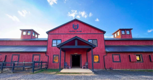 Red barn with a peaked roof and two upper windows, set against a blue sky with scattered clouds.