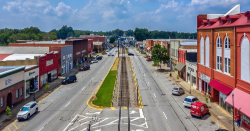 Aerial view of a small town street with shops, parked cars, and railway tracks running through the center.