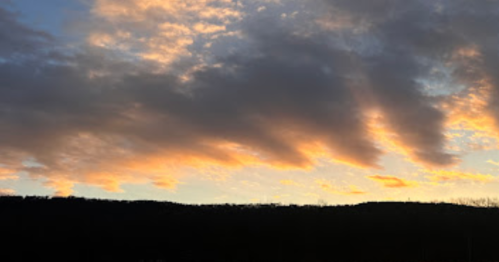 A colorful sunset with orange and yellow hues against a backdrop of dark clouds and a silhouette of hills.