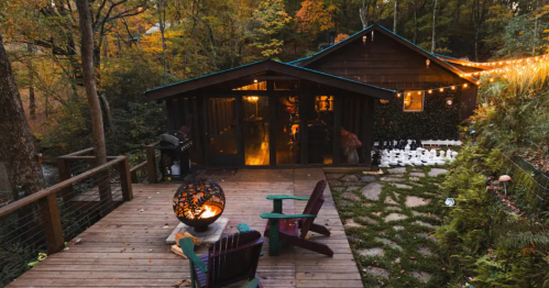 Cozy cabin surrounded by autumn foliage, featuring a fire pit and wooden deck with colorful chairs.