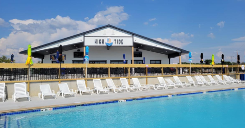 A pool area with white lounge chairs and a building labeled "High Tide" in the background under a blue sky.