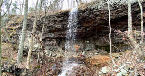 A waterfall cascading over rocky terrain, surrounded by trees and a forested area.