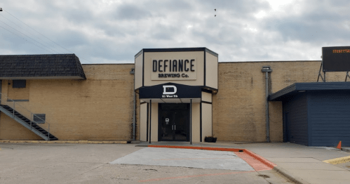 Exterior of Defiance Brewing Co. building with a sign and awning, featuring a cloudy sky in the background.