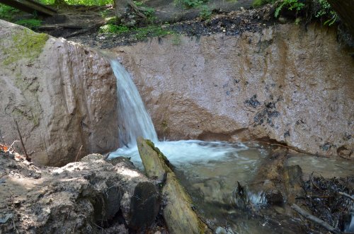 A small waterfall cascades over a rocky ledge into a serene pool surrounded by greenery.