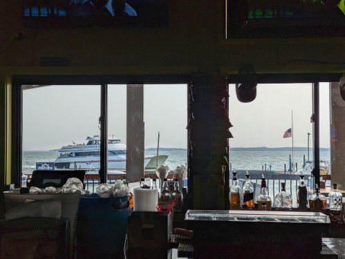 View from a bar window overlooking a boat on the water, with bottles and glasses in the foreground.