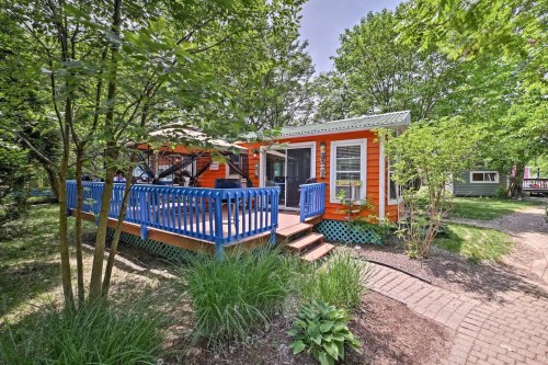 A colorful orange house with a blue porch, surrounded by greenery and trees, on a sunny day.