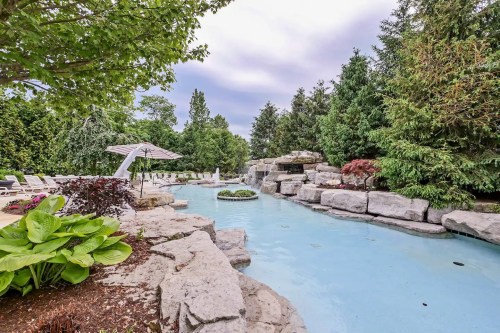 A serene pool area surrounded by lush greenery and rock formations, featuring lounge chairs and an umbrella.