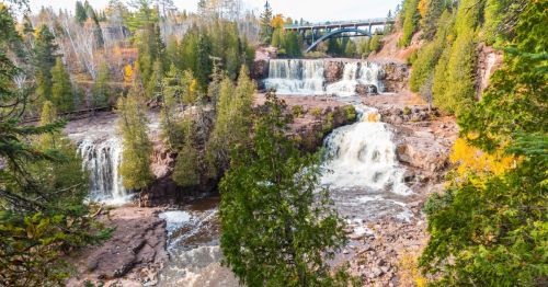 Aerial view of Middle Gooseberry Falls surrounded by rocks, tall trees, and a bridge in the background