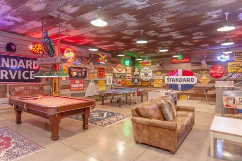 A vibrant game room featuring a pool table, ping pong tables, and vintage neon signs on the walls.
