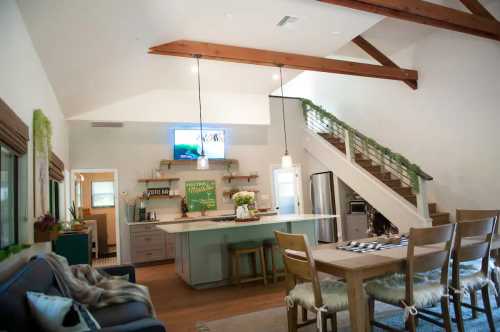 Bright, modern kitchen and dining area with wooden beams, a staircase, and cozy furnishings.