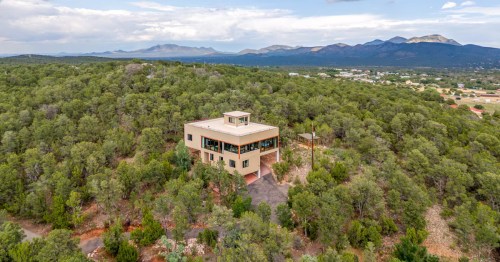An aerial view of a square home surrounded by a thick forest in New Mexico.