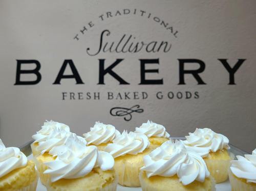 Cupcakes with white frosting in front of a sign for Sullivan Bakery, featuring "Fresh Baked Goods."