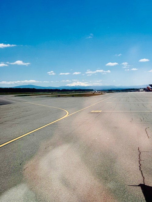 A clear blue sky over an airport runway, with distant mountains visible in the background.