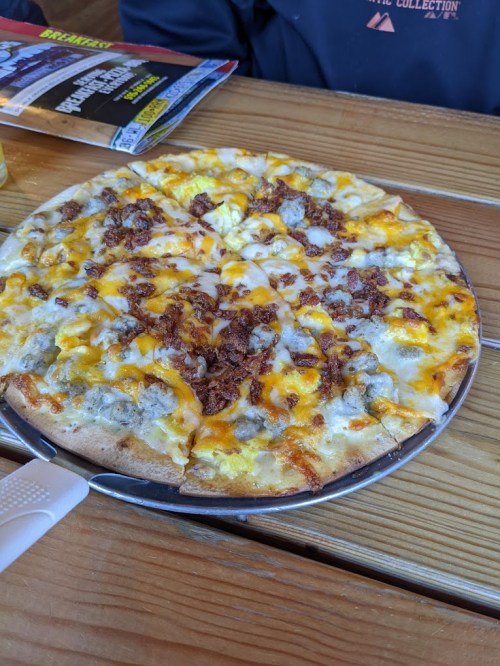 A freshly baked pizza topped with melted cheese, bacon, and a golden crust, served on a metal tray.