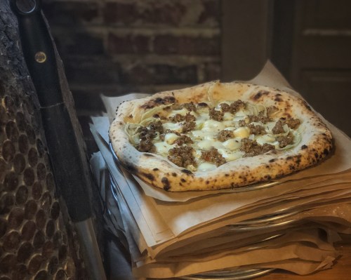 A freshly baked pizza topped with sausage and cheese, resting on a stack of parchment paper.
