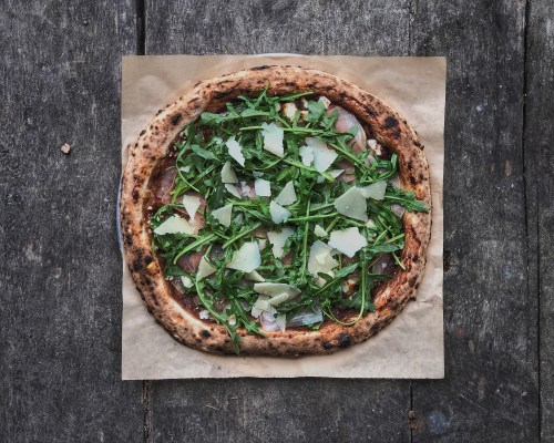 A freshly baked pizza topped with arugula and shaved cheese on a rustic wooden surface.