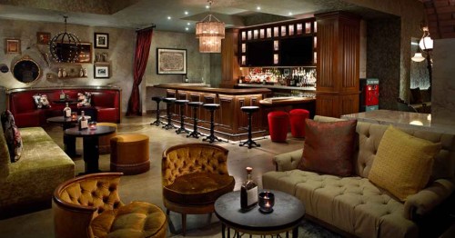 Moody Prohibition-era lounge at Pin + Proof in Louisville, KY, with plush seating and a dark wood bar.