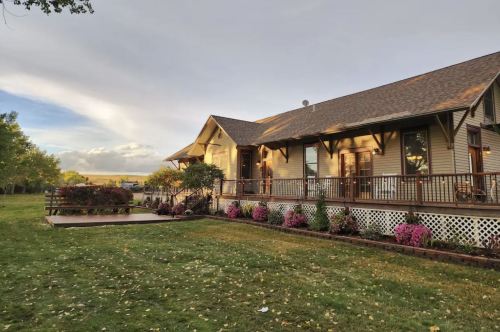 A charming house with a porch, surrounded by a well-maintained lawn and colorful flower beds under a cloudy sky.
