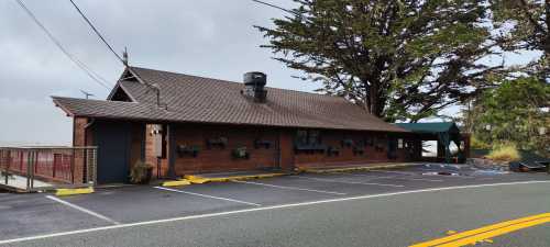 A rustic wooden building with a sloped roof, surrounded by trees, located along a quiet road.