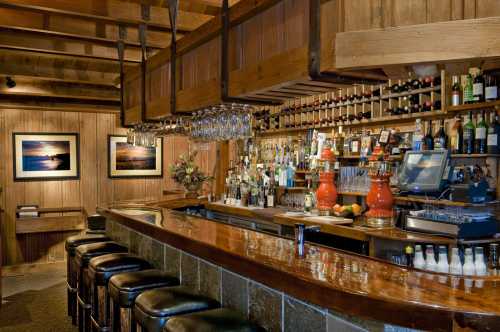 A cozy wooden bar with a polished counter, shelves of bottles, and framed photos on the walls.